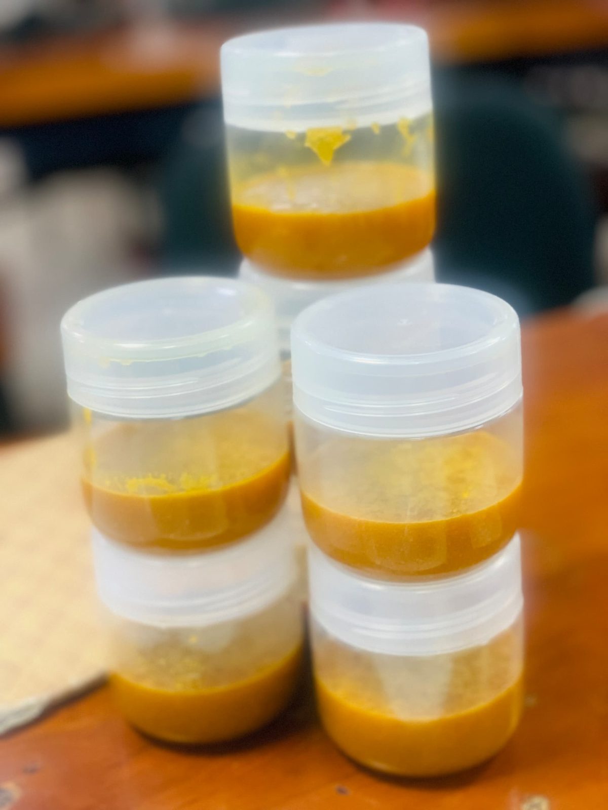 Three stacks of clear plastic containers filled with golden beeswax product on a wooden surface